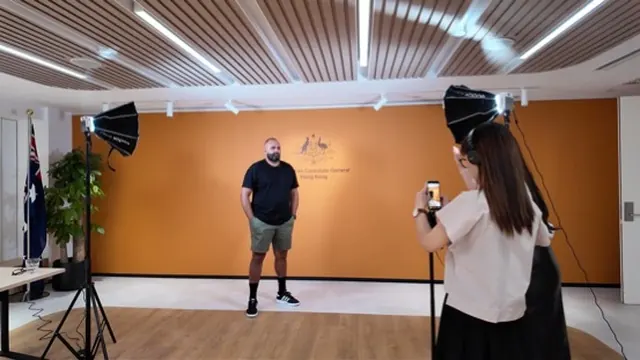 A studio shoot in progress in front of an orange wall, with lights and a photographer.