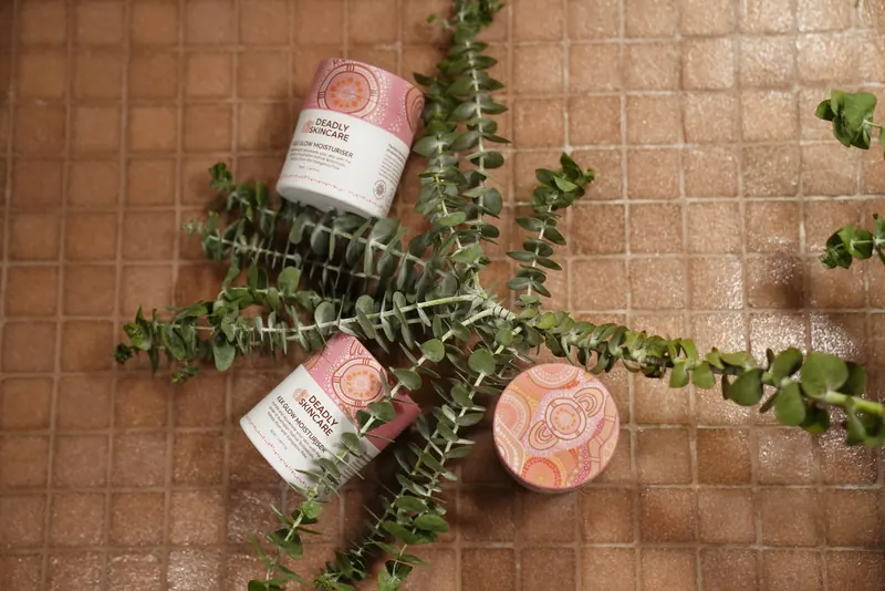 Deadly Skincare jars laid on terracotta tiles with banksia leaves, seen from above.