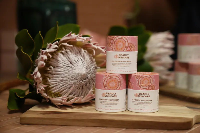Stacked Deadly Skincare jars beside a king protea on a wooden board.