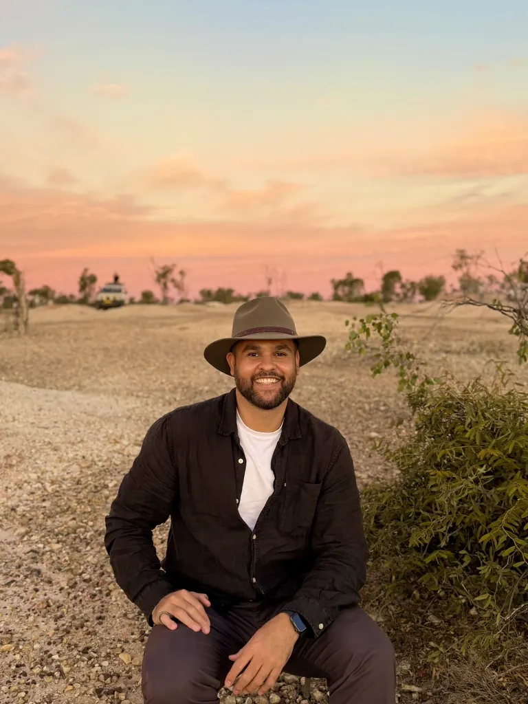 James Saunders, founder of Barragi Mawang, seated outdoors in a wide-brim hat at sunset.