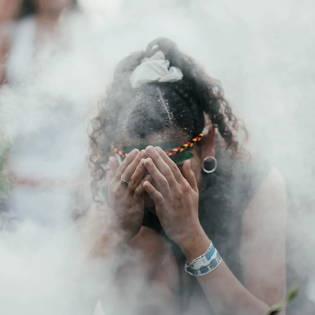 A woman covers her face with her hands, surrounded by smoke.