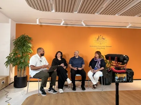 A panel of four seated in front of the orange wall of the Australian Consulate-General in Hong Kong.
