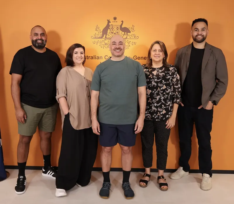 Five people standing together in front of the Australian Consulate-General crest.